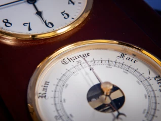Close-up: Vintage wood/brass weather station shows a barometer face with 'Change, Rain, Fair' below...