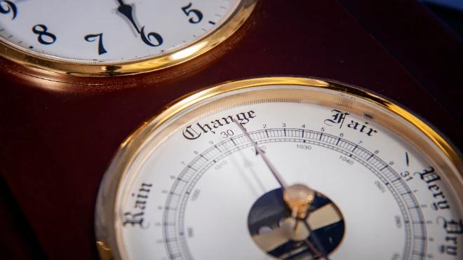 Close-up: Vintage wood/brass weather station shows a barometer face with 'Change, Rain, Fair' below...